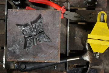 Forged steel decorative element resting on thick metal plate handmade anvil during blacksmith work on workshop background close up.