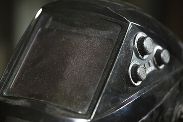 Protective welding mask visor with adjustment knobs showing worn transparent screen on industrial workshop background.