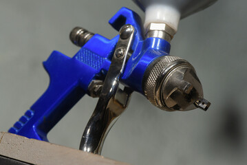 Blue HVLP spray gun nozzle with trigger and metal air cap close up on neutral background.