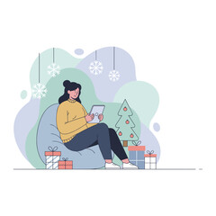 Young woman uses a digital tablet while relaxing on a beanbag chair near Christmas gifts and a tree Holiday shopping concept