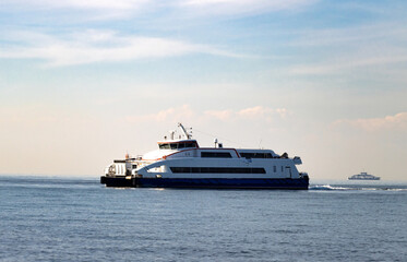 Naklejka premium Passenger car ferry crossing calm coastal waters with upper deck and vehicles—framed by distant vessel, soft sky, and maritime atmosphere in active transport route.