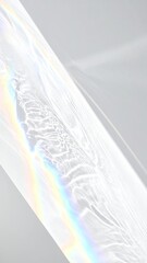Abstract diagonal light refraction pattern with subtle rainbow spectrum against a pale gray surface.