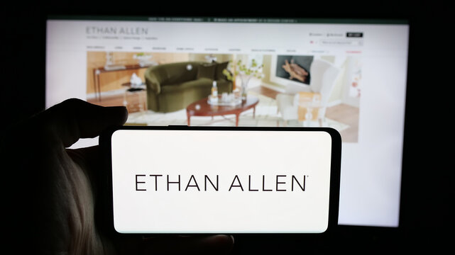 Stuttgart, Germany - 12-10-2025: Person holding cellphone with logo of furnishing company Ethan Allen Interiors Inc. on screen in front of webpage. Focus on phone display.