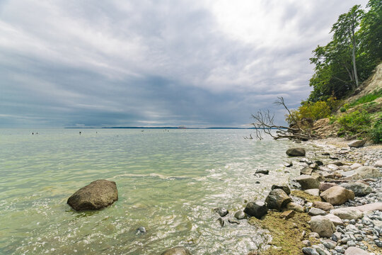 View of the tranquil, turquoise sea gently laps at a rocky shore beneath a dramatic, cloudy sky, Sassnitz, Mecklenburg-Vorpommern, Germany.