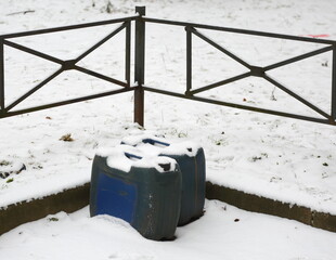 Two canisters are standing near the fence of a snow-covered lawn