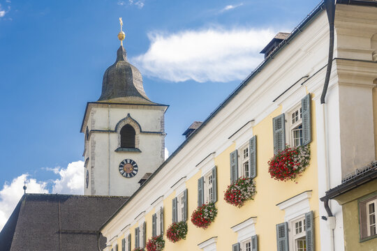 View of the white church tower rising against a blue sky, contrasted by the warm yellow walls with vibrant flower boxes, Saint Wolfgang im Salzkammergut, Upper Austria, Austria.