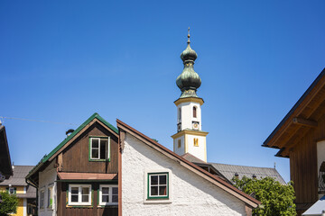 View of the architectural contrast of traditional buildings against the backdrop of a church tower under a clear blue sky, Saint Gilgen, Salzburg, Austria.