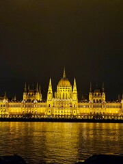Fototapeta premium Parliament glowing brightly at night in Budapest, Hungary. View across the Danube River.