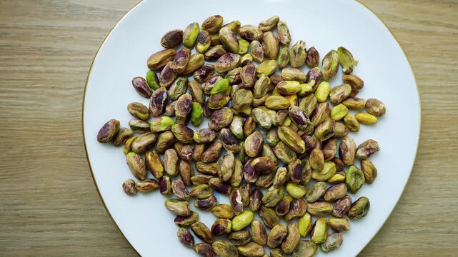 Unshelled Pistachios on a White Plate, White plate filled with unshelled pistachios on a wooden table