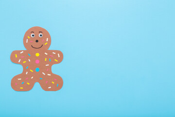Brown gingerbread man shape with colorful sprinkles created from application paper. Light blue table background. Pastel color. Making decoration element. Closeup. Empty place for text. Top down view.