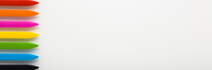 Colorful wax crayons on light gray table background. Closeup. Wide banner. Empty place for text. Top down view.