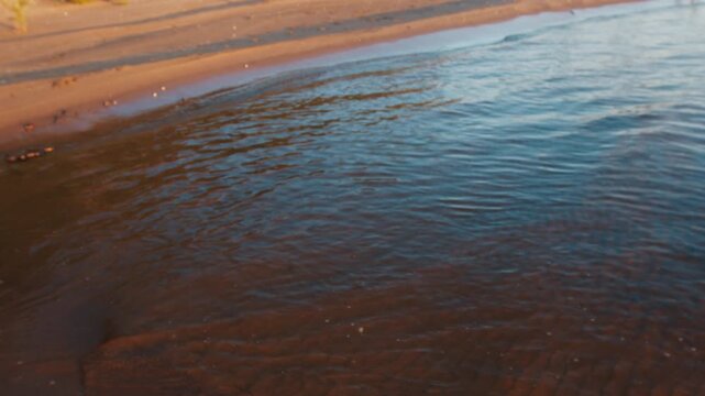 Lake with gentle calm waves rolling over the sandy beach during sunset