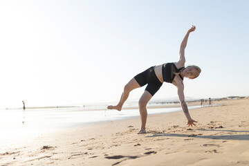 Woman balancing in half moon pose on sunny beach