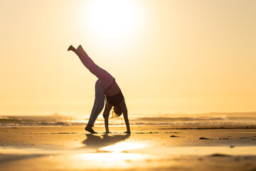 Woman practicing capoeira handstand on beach at sunset