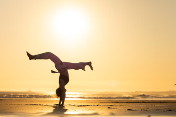 Woman practicing capoeira handstand on beach at sunset