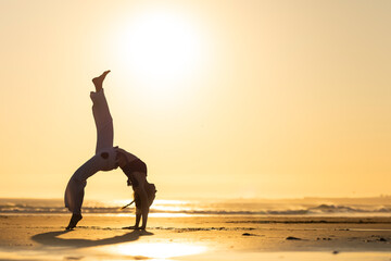 Woman practicing capoeira bridge pose on beach at sunset