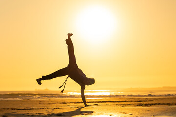 Man performing capoeira handstand on beach at sunset