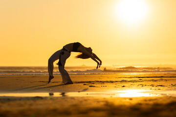 Capoeira artist performing flexible movement on beach at sunset