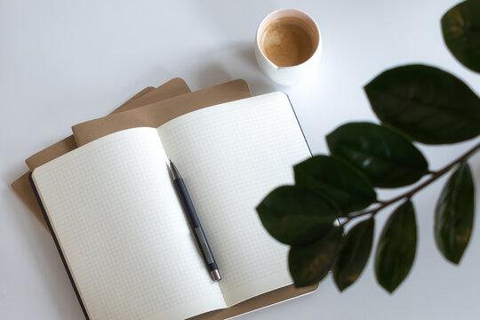 minimal flat lay workspace with notebooks, pen, coffee cup on white desktop background. home office aesthetics 