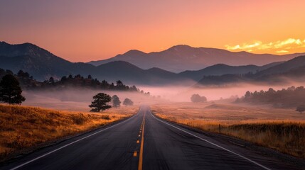Empty road leading through a misty mountain valley at sunrise with golden fields