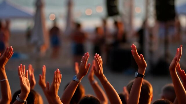 A crowd of people clapping hands in applause at a live music concert festival on the beach during a beautiful sunset. 4k video footage of audience appreciation and energy. 