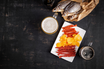 Beer and snack, chips and kabanos on a dark background.