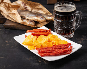 Beer and snack, chips and kabanos on a dark background.