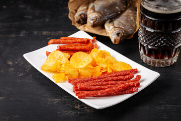 Beer and snack, chips and kabanos on a dark background.