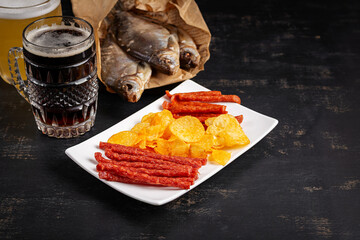 Beer and snack, chips and kabanos on a dark background.