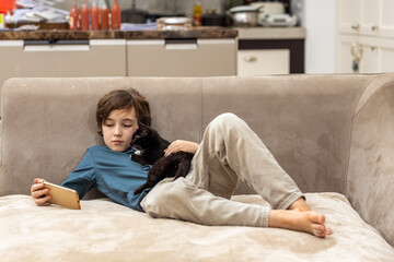 Boy playing with black kitten on sofa at home