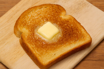 Toasted bread with melting butter on a wooden board presenting warm breakfast comfort food rustic styling and classic homemade morning meal