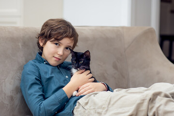 Boy playing with black kitten on sofa at home © Валентина Хруслова