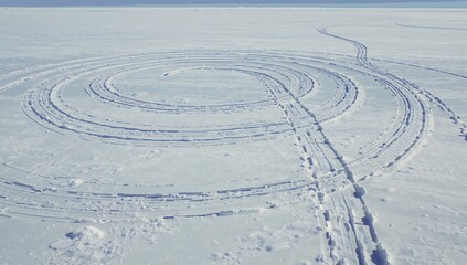 Forming concentric snow tracks carving rings on frozen lake, showing parallel ruts and snow blocks