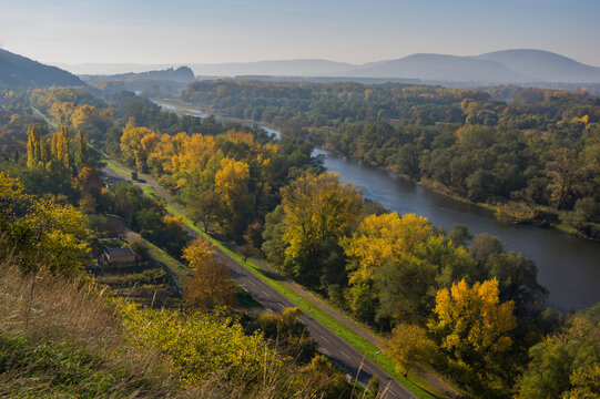 Aerial view of the Morava River flowing through a tapestry of autumnal trees near Devinska Nova Ves, where gold and green hues meet the water's edge, Devinska Nova Ves, Bratislava Region, Slovakia.