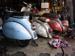 Fototapete Roller Old vintage scooter motorcycle in blue, white and red parked on a double stand in a workshop environment.  © ahmadjaa