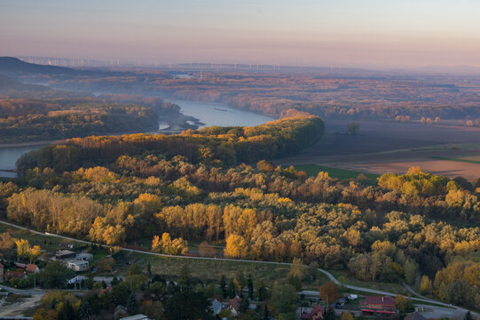 Aerial view of a tranquil river winding through a tapestry of autumn-hued trees, framed by the distant horizon, Devinska Nov&aacute; Ves, Bratislava Region, Slovakia.
