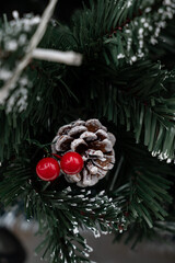 Christmas Decor: A detailed shot of festive elements on an evergreen tree, featuring a snow-dusted pinecone, two vibrant red berries.
