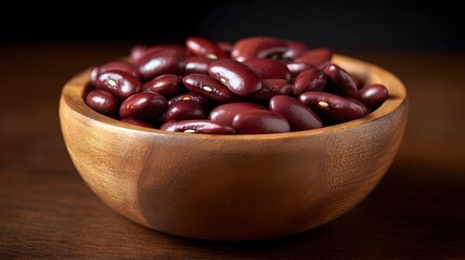 Close up of dark red kidney beans piled high in a rustic wooden bowl set against a dark moody background