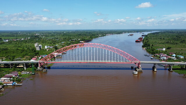 Aerial view of a tugboat pulling a barge filled with coal across the Rumpiang Bridge in the waters of South Kalimantan, Barito River