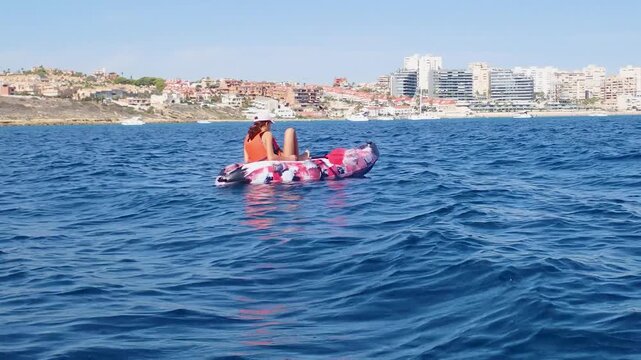 Young girl wearing a baseball cap sitting on a kayak in the calm waters of San Juan bay in Alicante Spain during a sunny summer day