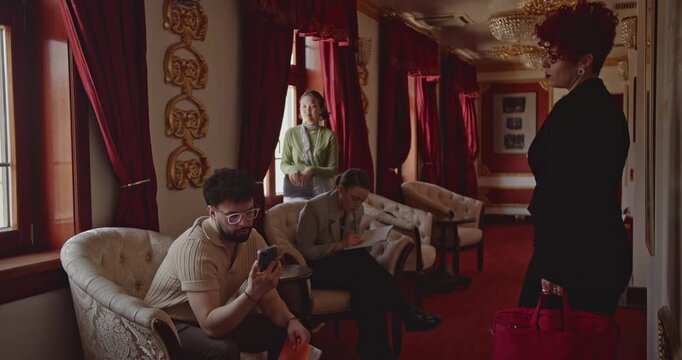 Business professionals prepare for a meeting in an elegant, traditional hotel lobby. One person talks on the phone, another writes, and a third looks out the window.