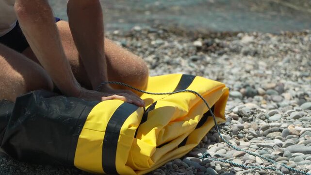 Man, packing, boat, rolling up inflatable dinghy on sunny rocky beach.