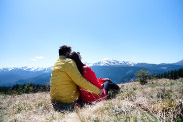 Two hikers taking a break on a mountain ridge. Sporty couple with hiking backpacks standing on background of snowy mountains.