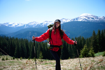 Female hiker with backpack and trekking poles walking in the mountains. Adventure lifestyle in nature. Active woman exploring forest trails on a sunny day.