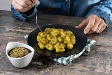Woman eating gnocchi with pesto sauce on rustic wooden table