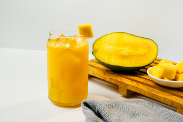 a glass of mango juice with ice cubes with a few mango slices and water in a glass bottle and empty space on the left. healthy drink concept.