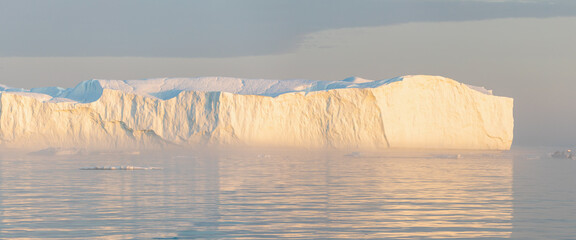 Little red sailboat cruising among floating icebergs in Disko Bay glacier during midnight sun season of polar summer. Ilulissat, Greenland. Unesco world heritage. Global warming and climate change.