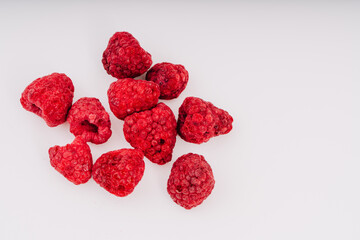 Freeze-dried raspberries scattered on a clean white surface, showcasing their vibrant red color and unique texture, perfect for healthy snacks or culinary creations with copy space