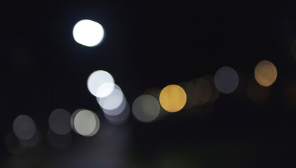 Blurred night illumination forms a diagonal sequence of bokeh circles on a dark background. Cool