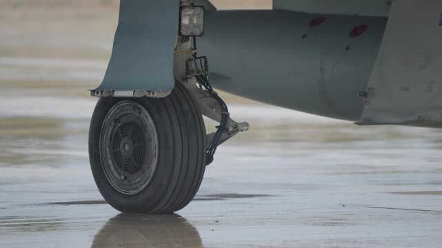 Detailed view of aircraft landing gear strut and wheel during servicing on wet airbase tarmac